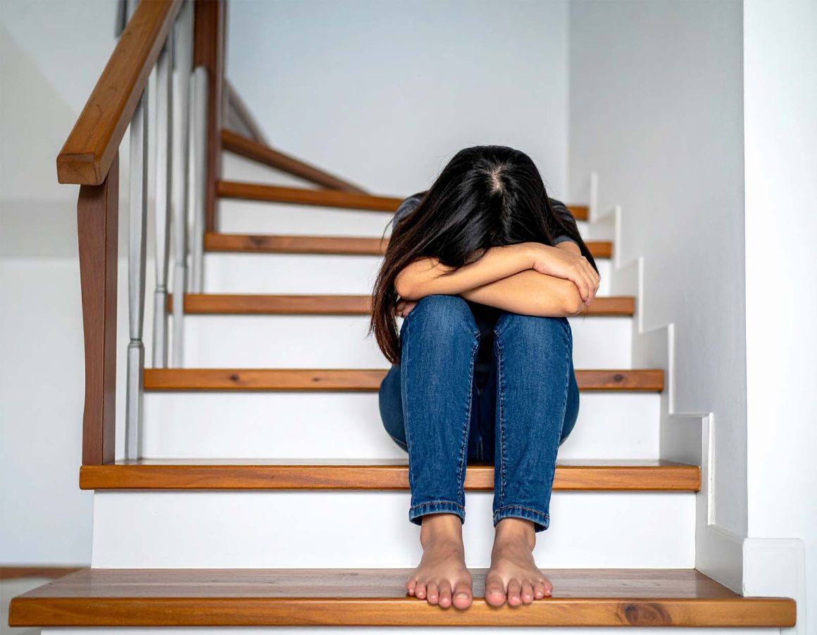 A girl sits on the stairs with her head in her hands