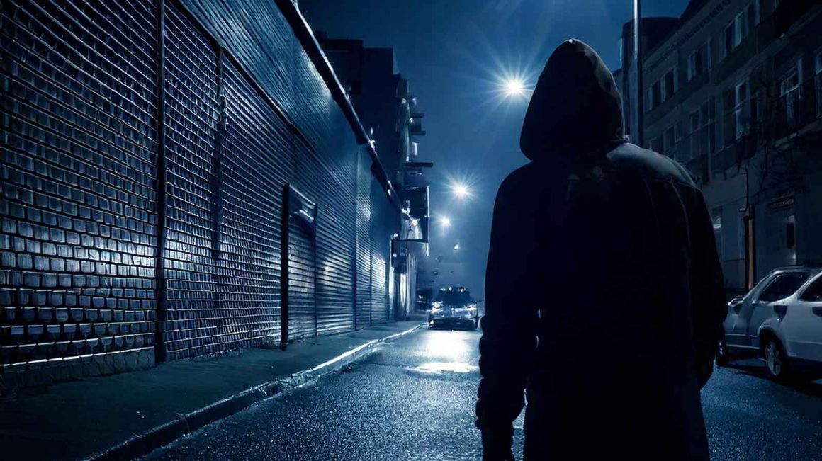 A hooded figure on a deserted street at night